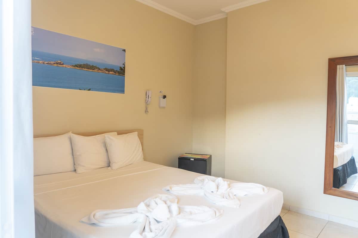 A hotel room with a bed, a painting of a coastal scene, a telephone, and a mirror.