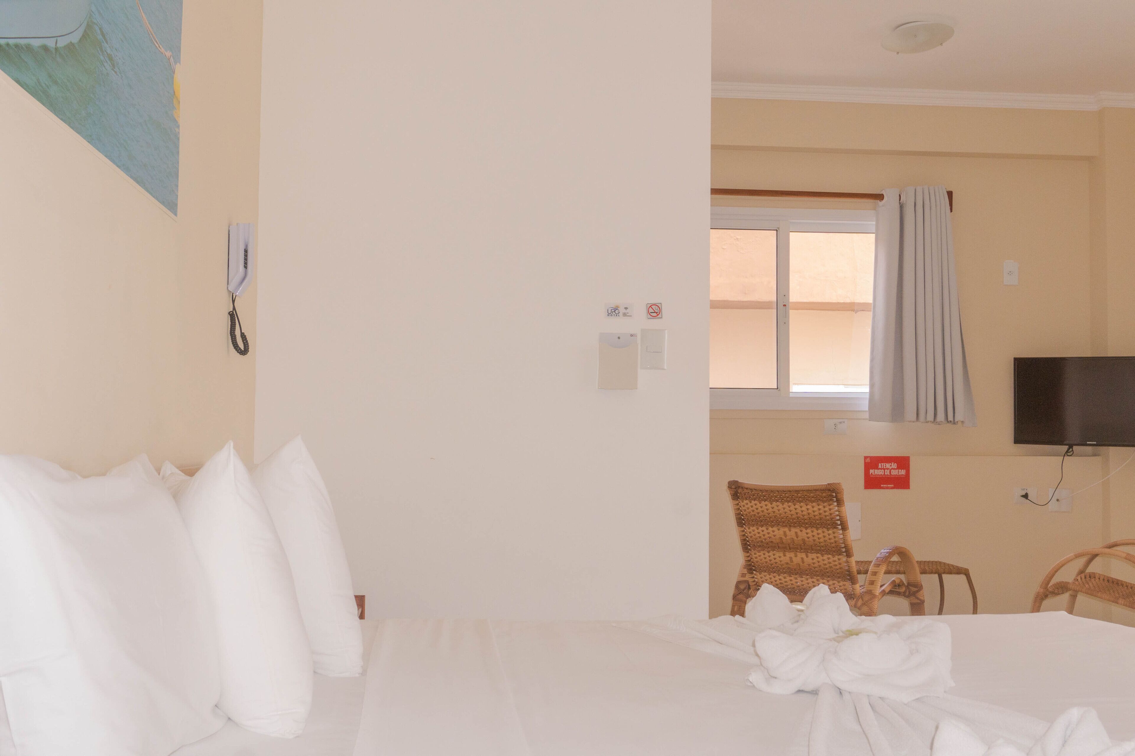 A hotel room with a bed, a television, a window with curtains, a chair, and a sign indicating a smoking area.