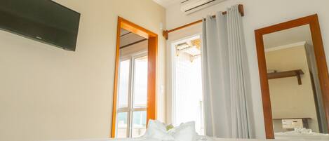A hotel room with a bed, an air conditioning unit, a flat-screen TV, and a large mirror.