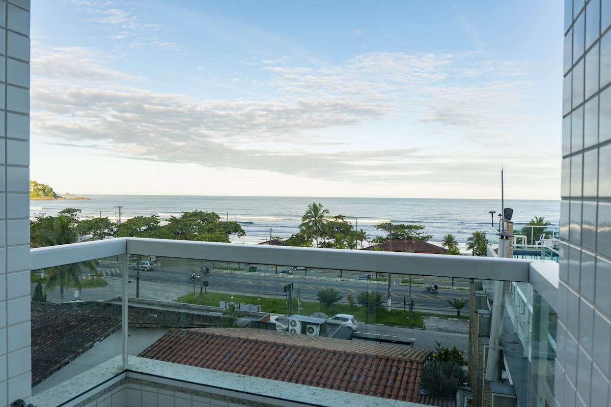 A view from a balcony overlooking a coastal road with palm trees and a clear sky.