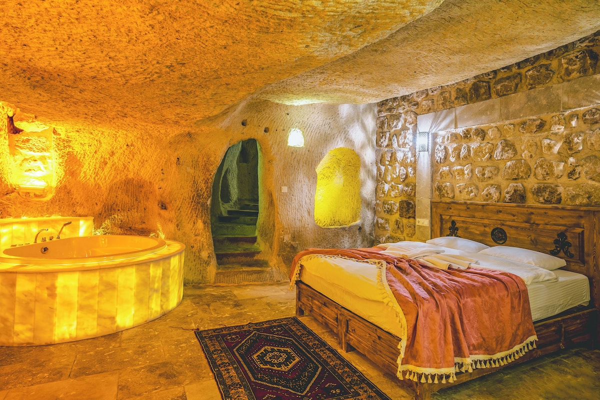 A room with a stone wall, a wooden bed, a stone bench, and a bathtub.