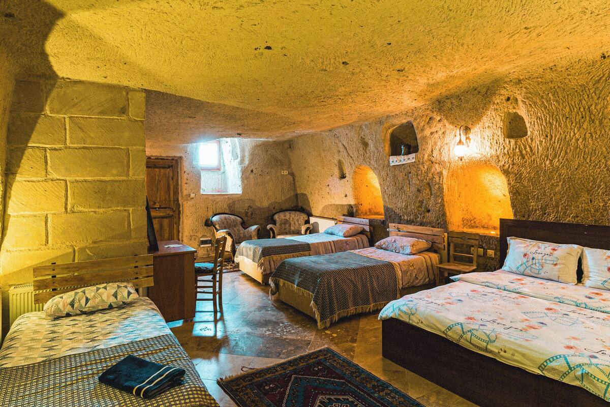 A rustic room with stone walls, two beds with patterned bedding, a wooden chair, and a small table.
