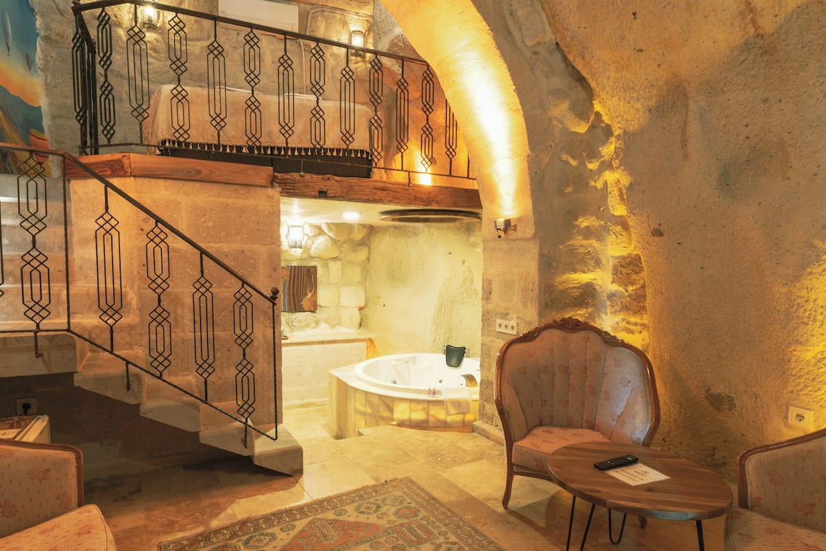 A spacious living area with a high wooden staircase, a round wooden coffee table, and a patterned rug.
