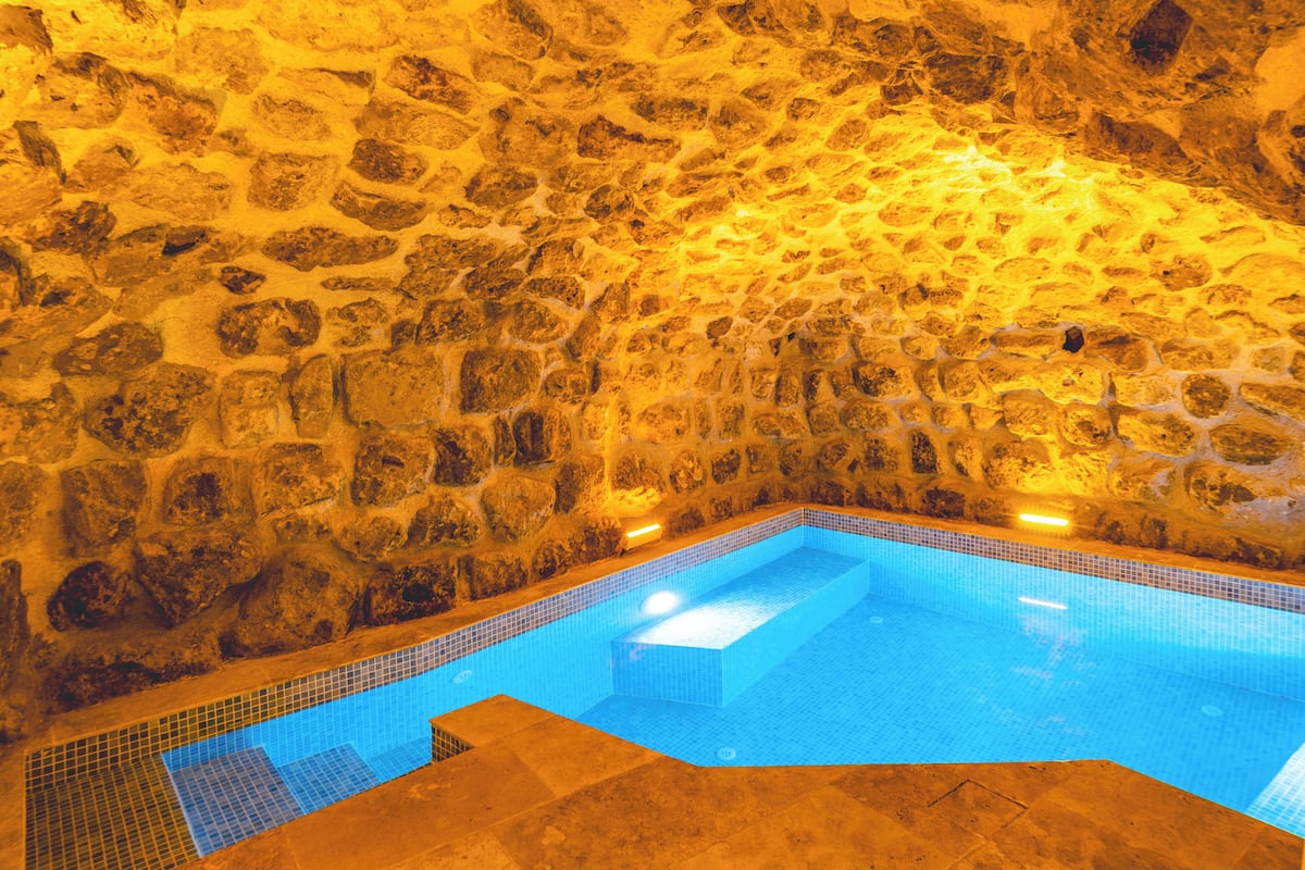 A stone-walled indoor pool with clear blue water and a tiled floor.