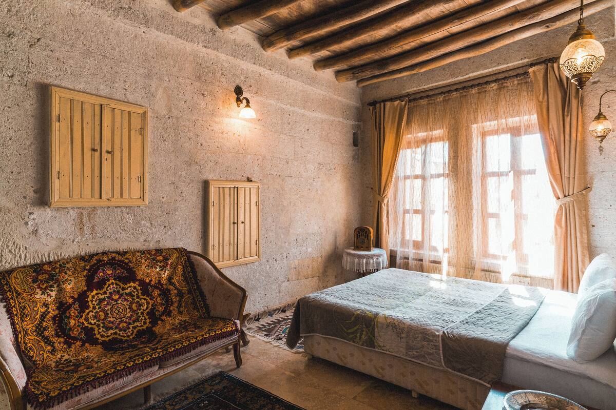 A traditional room with a wooden ceiling, a bed, a sofa, and a window with curtains.