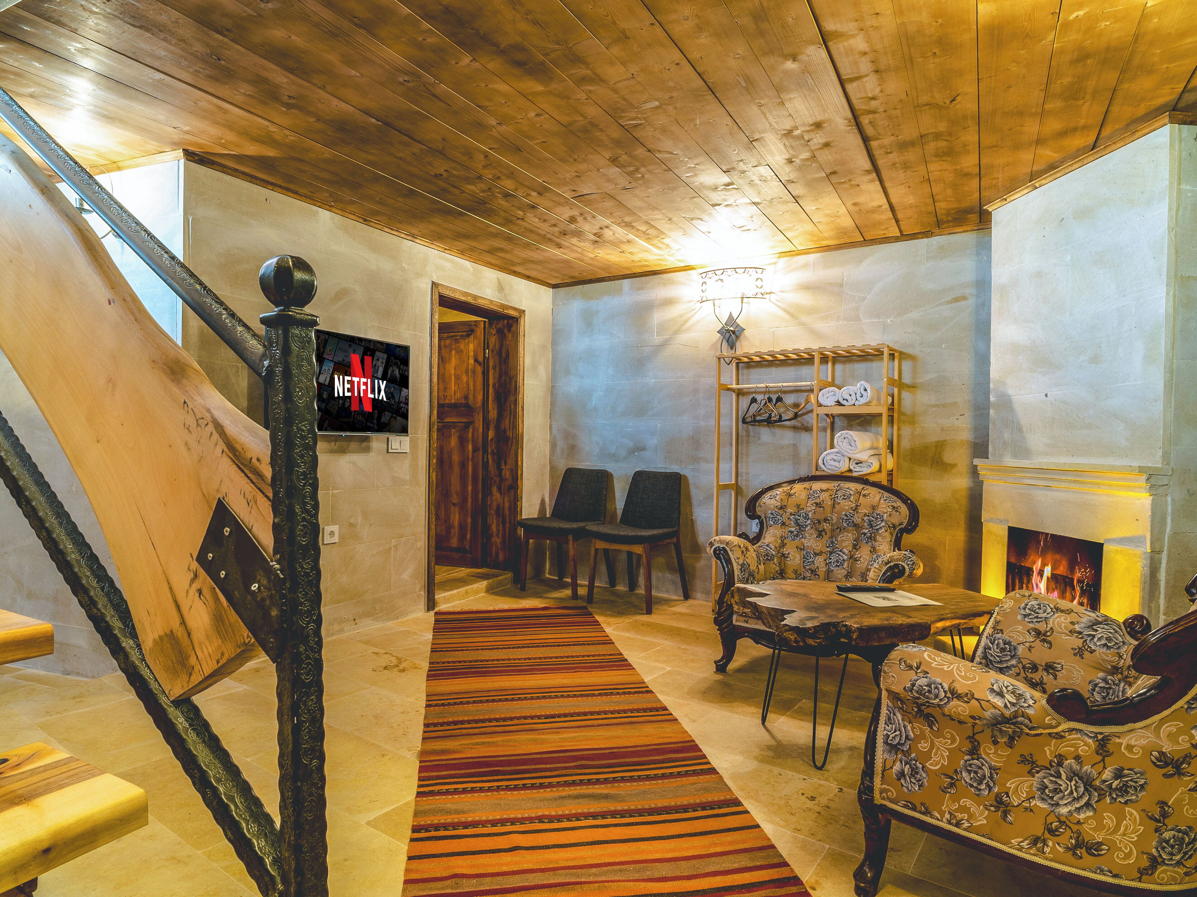 A cozy room with a wooden ceiling, a fireplace, a Netflix sign, and a patterned rug.