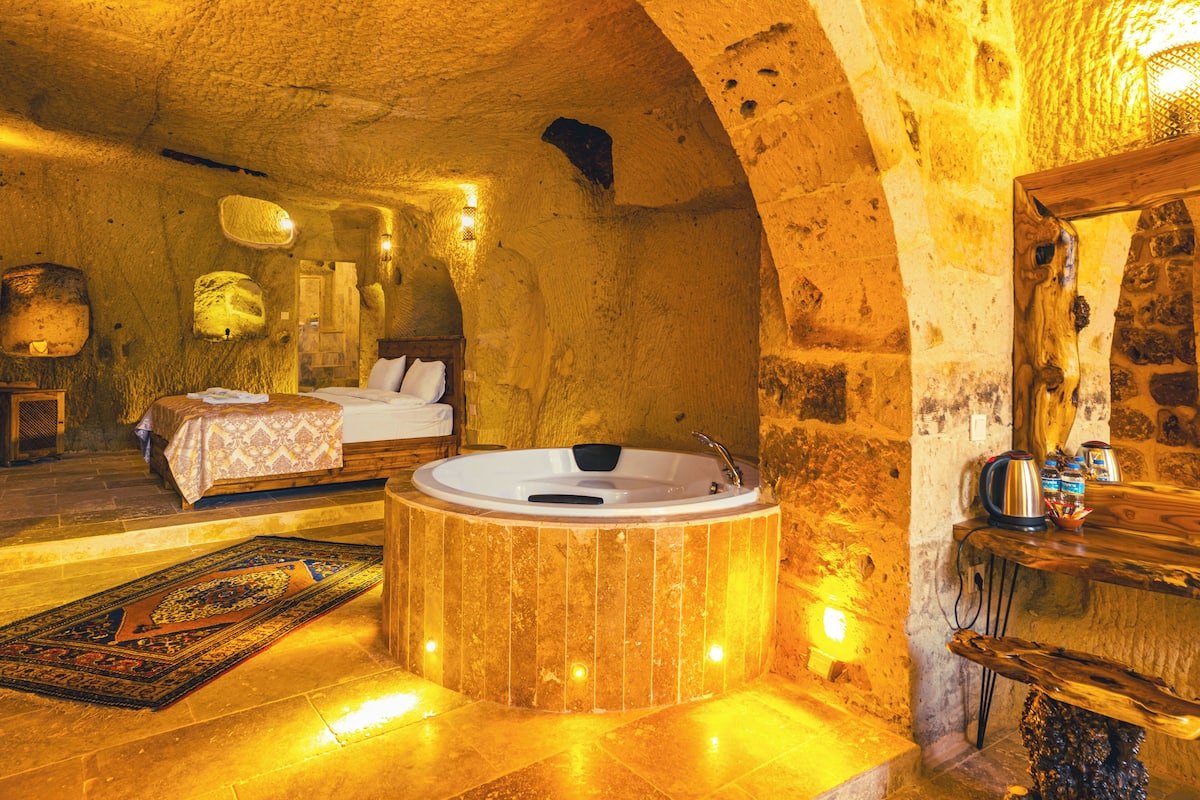 A luxurious room with a large wooden bathtub, a bed with white linens, and a stone wall.