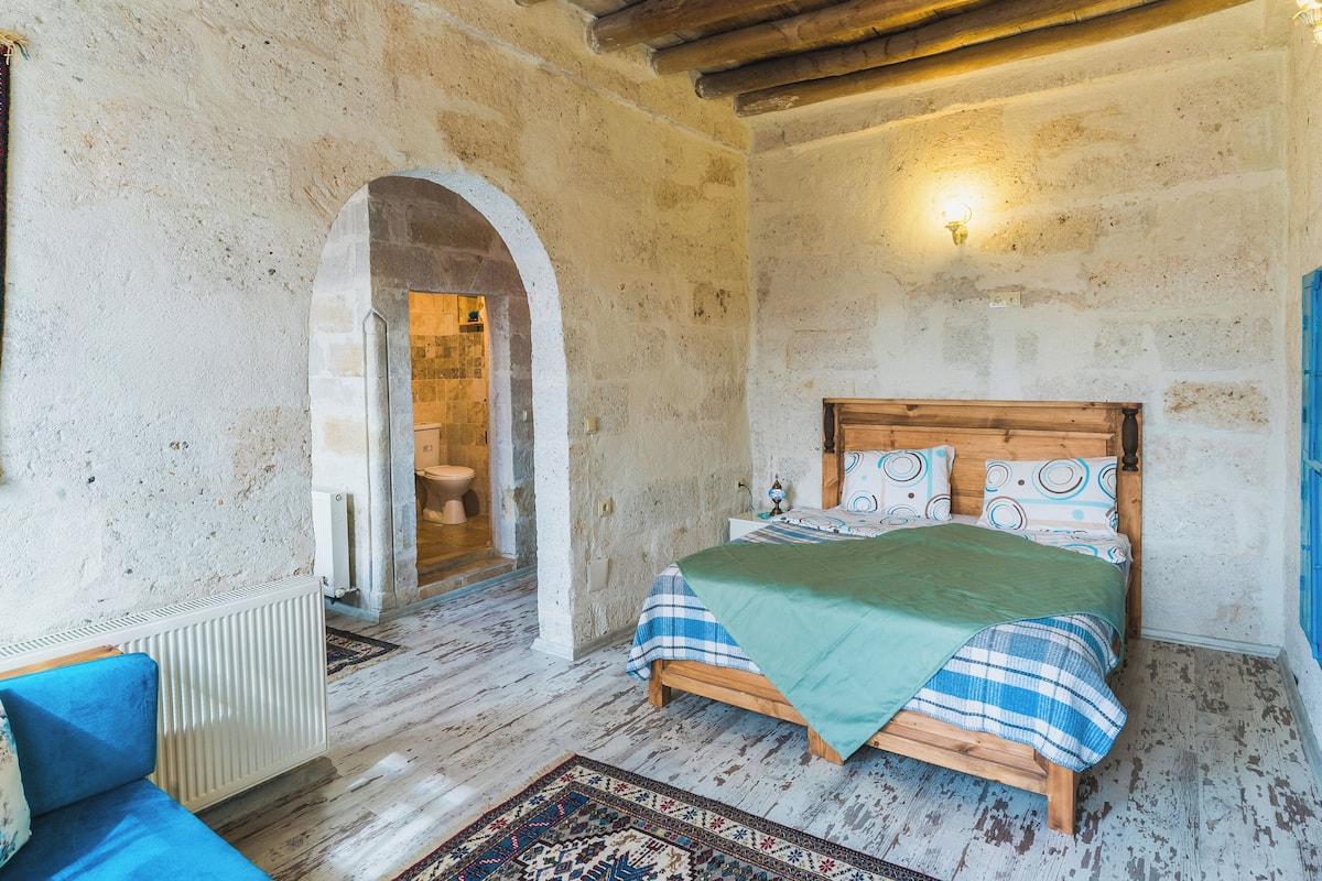 A rustic bedroom with a wooden bed, a blue sofa, and a stone wall.