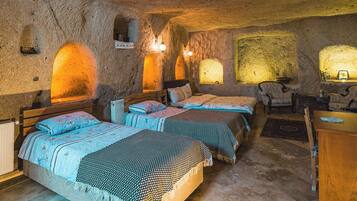 Una habitación rústica con tres camas, una silla de madera y paredes de piedra.