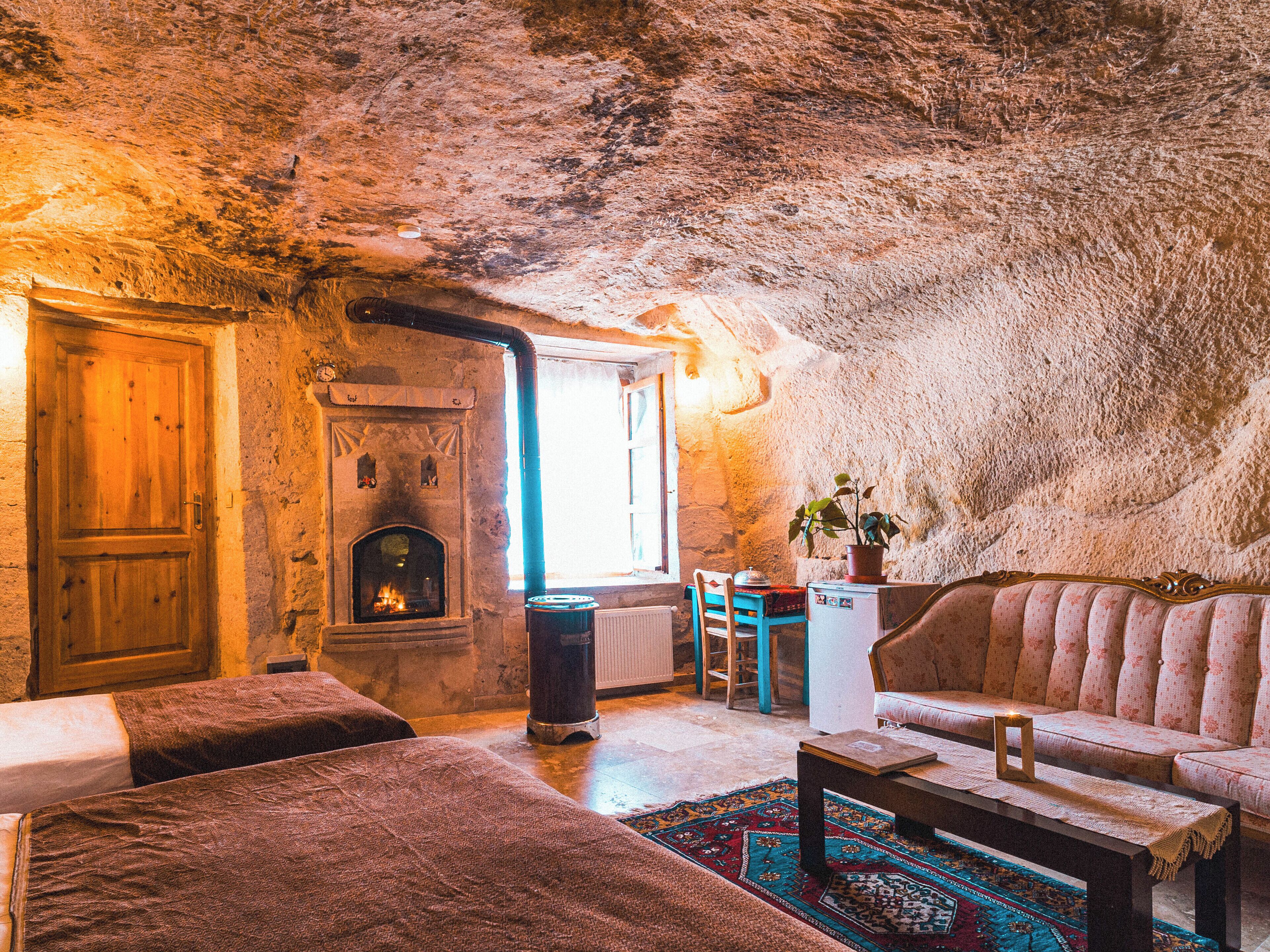 A cozy, rustic room with a stone wall, a fireplace, a sofa, and a dining table.