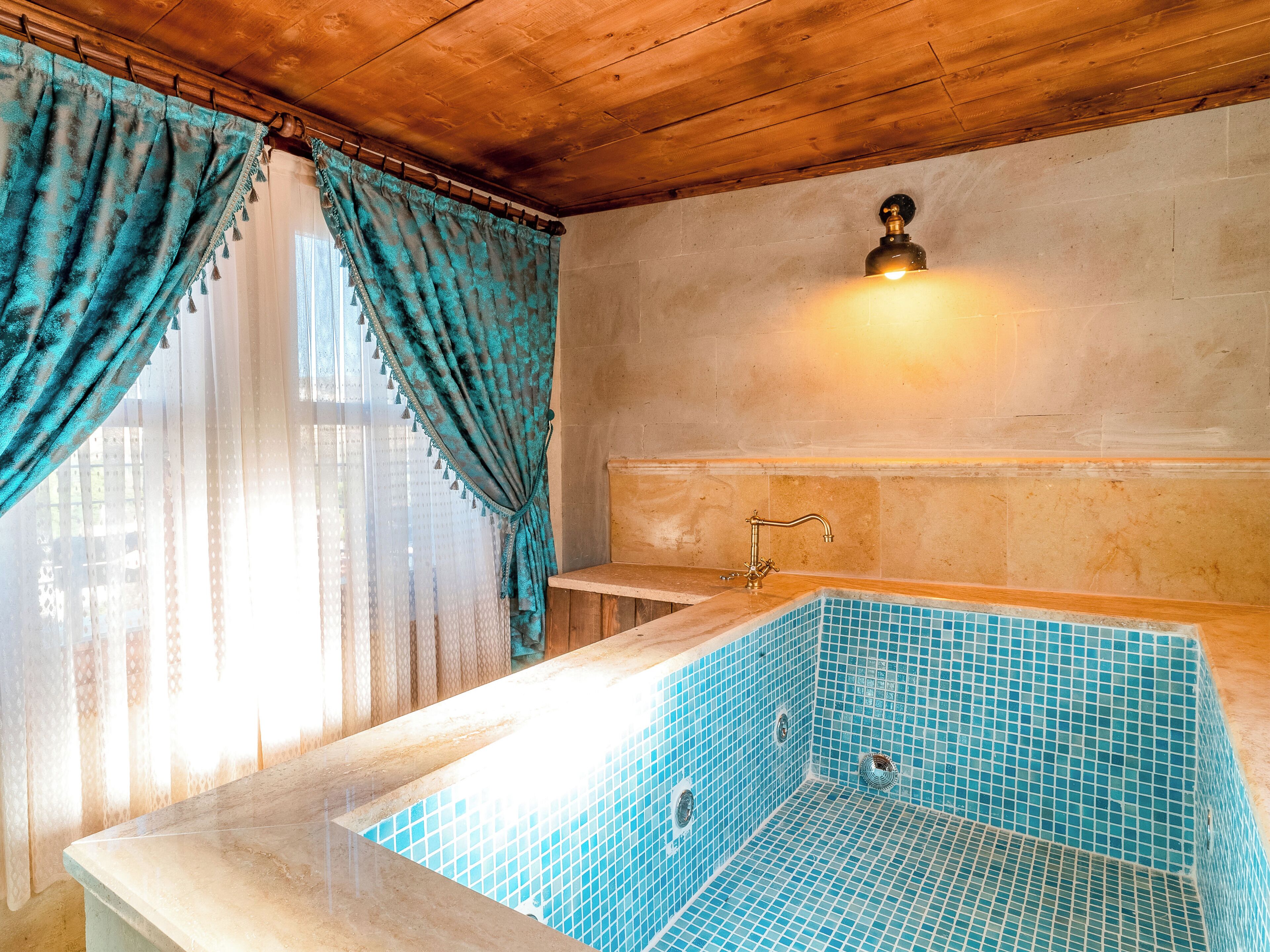 A bathroom with a blue-tiled bathtub, wooden ceiling, and a wall-mounted light fixture.