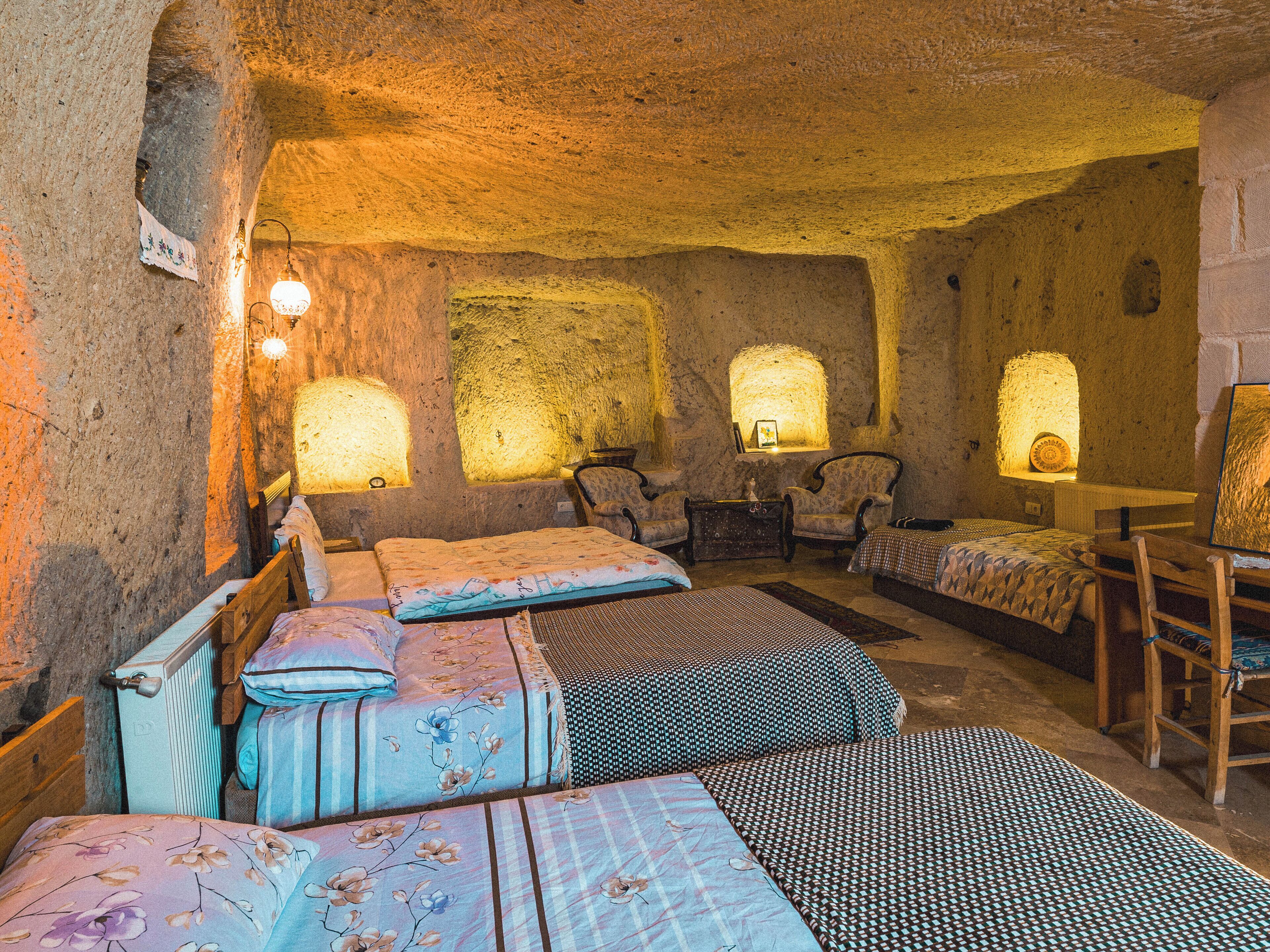 Una habitación rústica con paredes de piedra, varias camas con ropa de cama floral y geométrica, y lámparas fijadas a la pared.