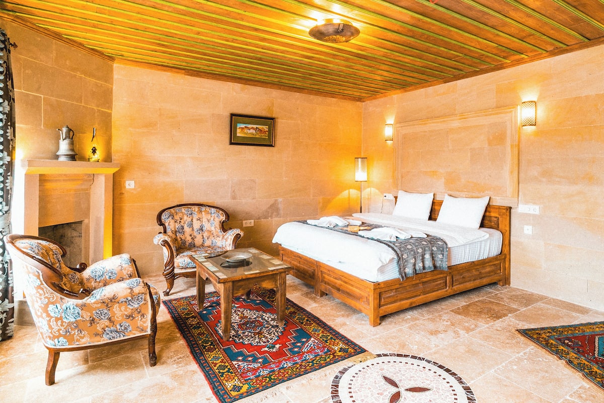 A cozy bedroom with a wooden bed, two chairs, a small table, and a fireplace.
