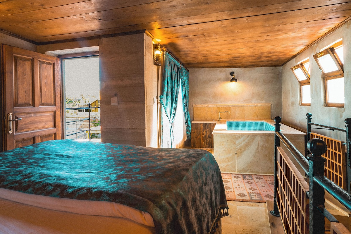 A bedroom with a large bed, wooden ceiling, and a bathroom with a window.