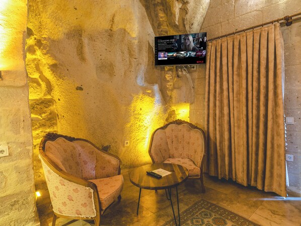 A room with a stone wall, two upholstered chairs, a small round table, and a television mounted on the wall displaying a Netflix interface.
