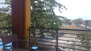 A balcony with wicker chairs and a table, overlooking a construction site with trees and a clear sky. - Sinar Harapan (Tomia Island)
