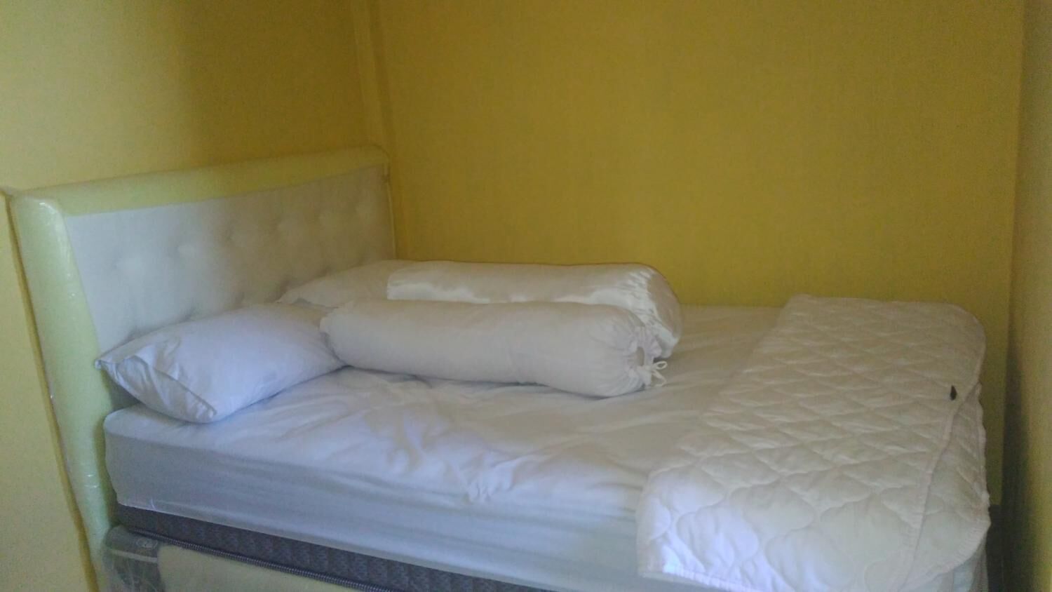 Een bed met witte beddengoed en kussens in een kamer met gele muren.