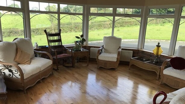 A sunlit room with a wooden floor, wicker furniture, and large windows offering a view of a green landscape. - Kilcreeny Lodge (Lisburn)