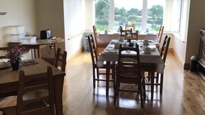 A dining area with a large window, wooden table, chairs, and a small kitchen area with a toaster and containers. - Kilcreeny Lodge (Lisburn)