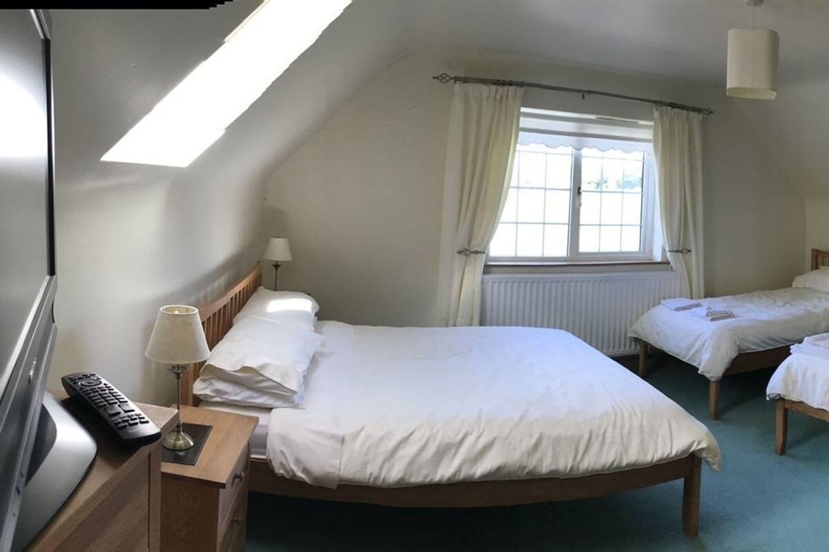 A bedroom with a single bed, a desk with a lamp, a radiator, and a window with curtains.