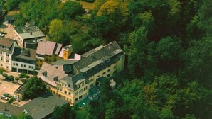 An aerial view of a residential area with multiple houses, surrounded by dense greenery and a circular park with a fountain. - Burghotel Volmarstein (Wetter)