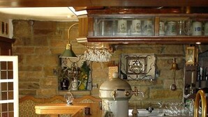 A rustic kitchen with a stone wall, wooden bar stools, a vintage espresso machine, and a hanging light fixture. - Burghotel Volmarstein (Wetter)