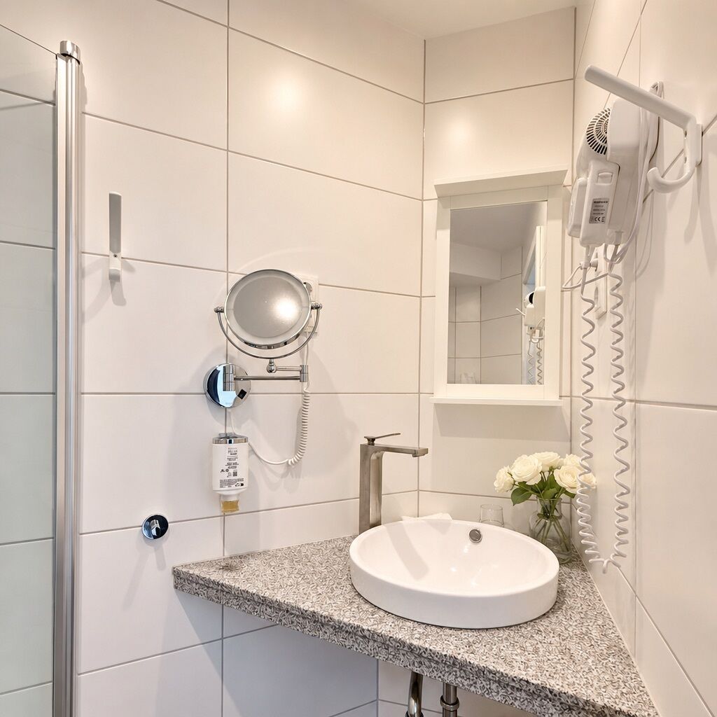 A modern bathroom with a white sink, a mirror, a hairdryer, and a shower.