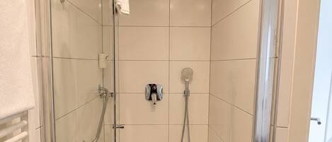 Un baño moderno con puerta de vidrio, un cabezal de ducha de mano, un cabezal de ducha empotrado y un perchero para toallas.
