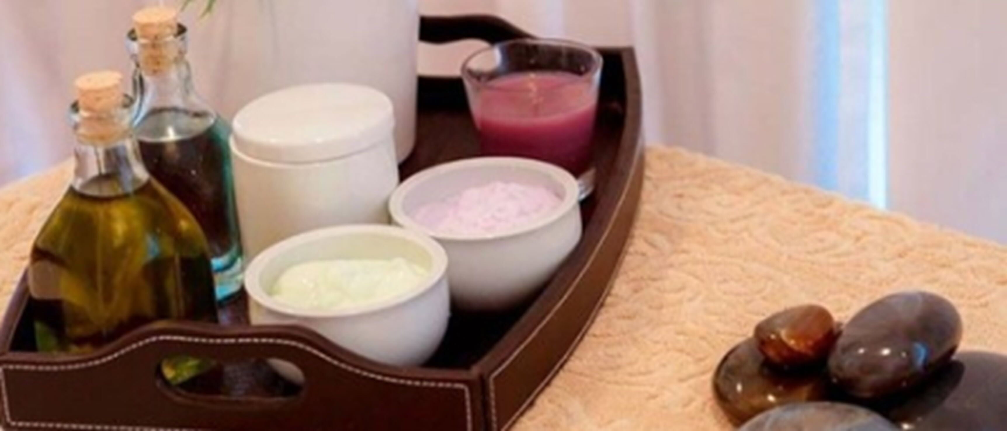 Un plateau contenant divers produits de spa, notamment des flacons, des bols et un verre rempli d’un liquide rose.