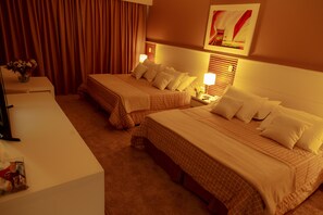 A hotel room with two beds, a desk, and a chair. There is a vase with flowers on the desk. - Vale Suiço Resort (Itapeva)