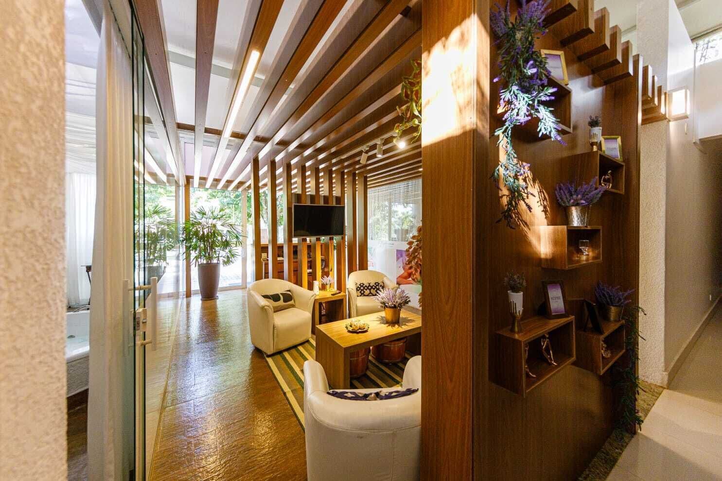 Uma sala de estar moderna com sofá, poltronas, mesa de centro e televisão. Há estantes de madeira com plantas e objetos decorativos.