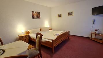 A bedroom with a wooden bed, bedside tables, a desk with a chair, and a TV mounted on the wall.