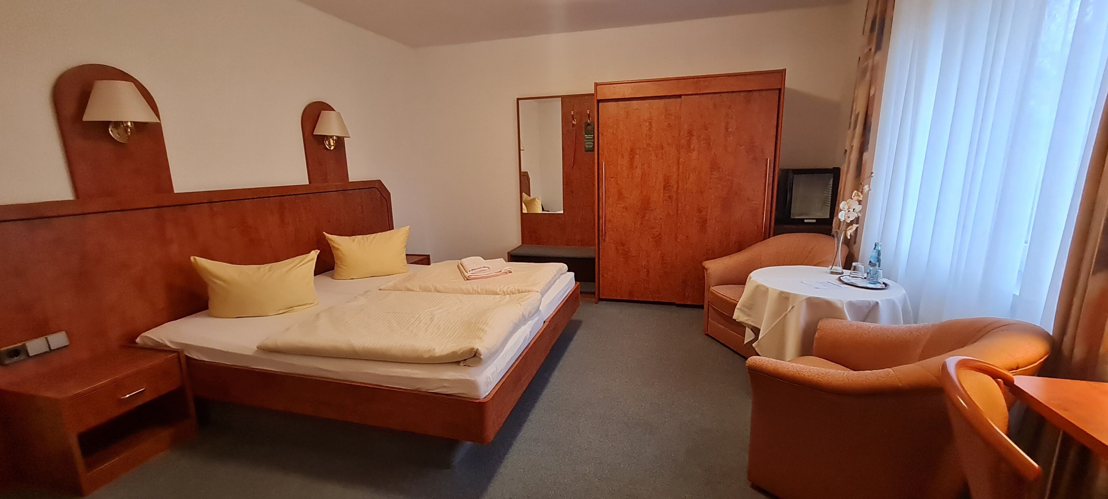 A hotel room with a bed, bedside tables, a desk, a chair, a television, and a wardrobe.