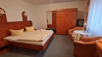 A hotel room with a bed, bedside tables, a desk, a chair, a television, and a wardrobe.