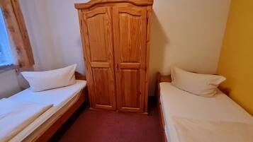 Una habitación pequeña con dos camas individuales, un armario de madera y una ventana con cortinas.