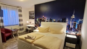 A hotel room with a bed, a desk, a chair, and a cityscape mural on the wall. - Hotel Prox (Arnstadt)