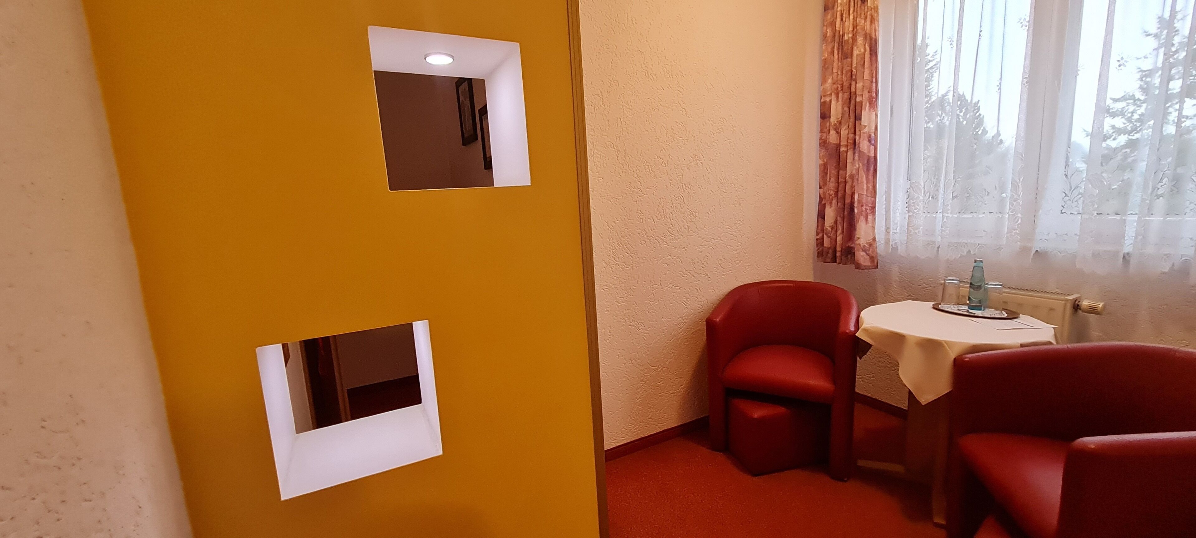 A room with two red chairs, a small table, and a window with curtains.