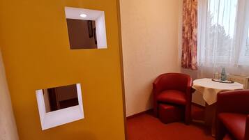 A room with two red chairs, a small table, and a window with curtains.