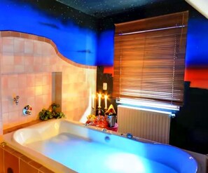 Un baño con bañera, una ventana con persianas y una pared con diseño de estrellas.