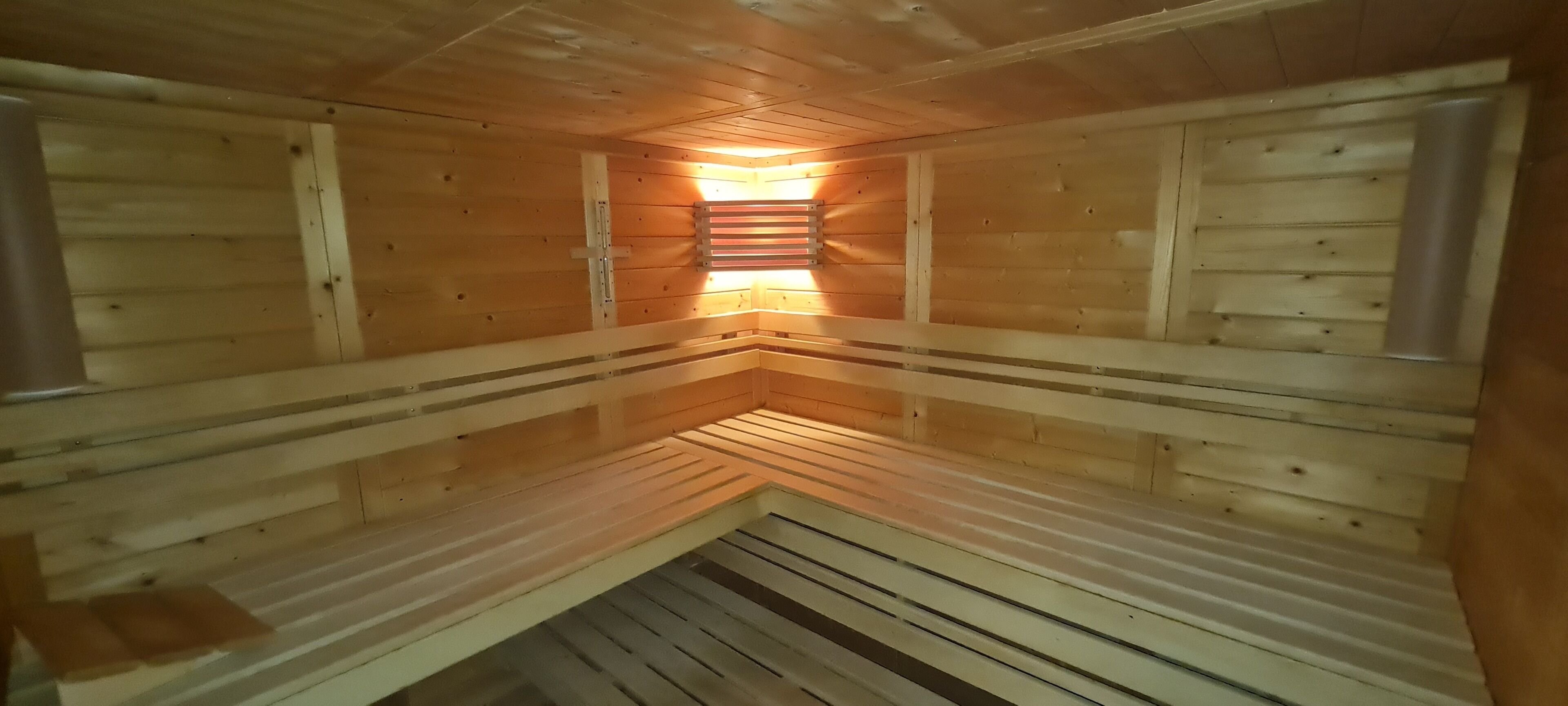 En sauna med træbænke placeret i et hjørne, en midterbænk og et skråt loft.