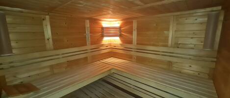 Una sauna con bancos de madera dispuestos en un rincón, un banco central y un techo inclinado.