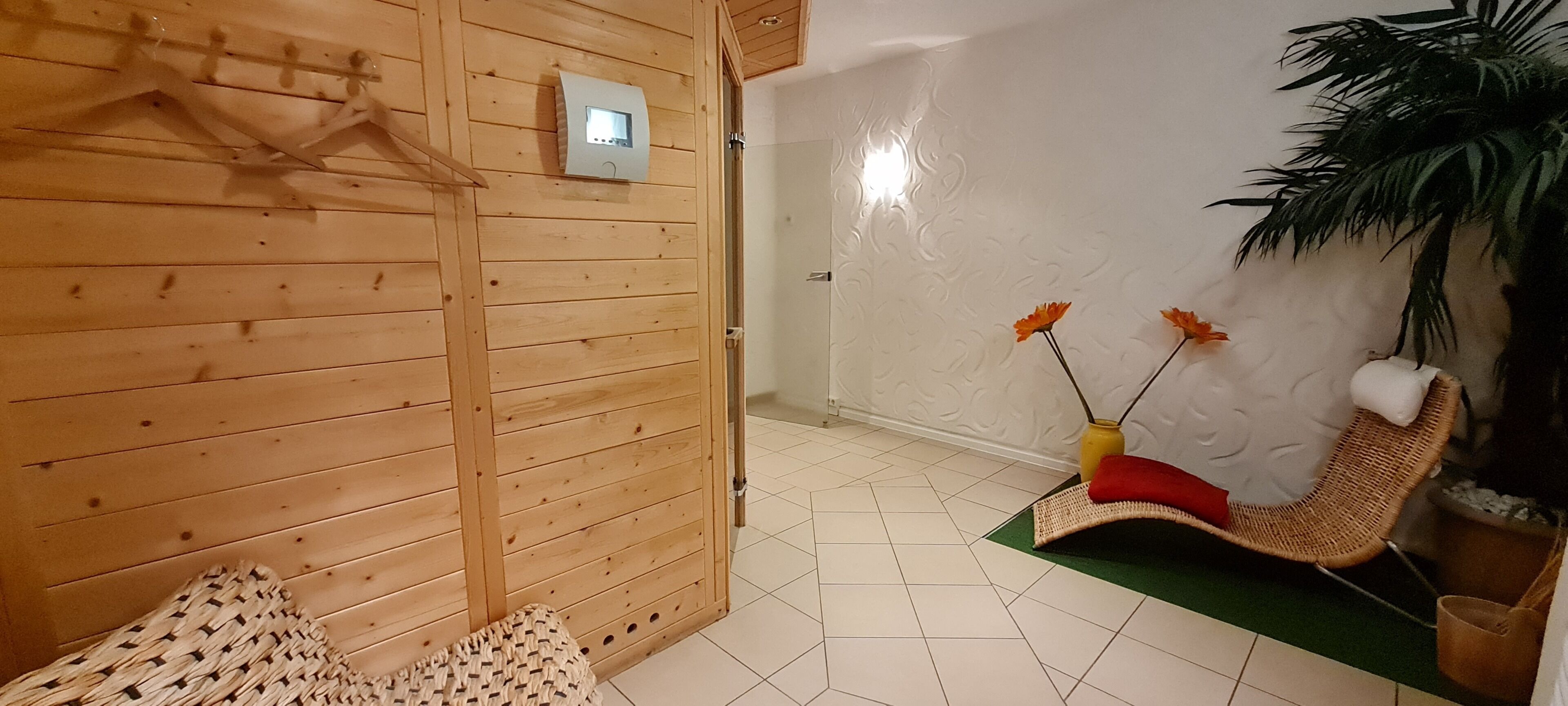A wooden-paneled room with a bench, a chair, a wall-mounted heater, and a potted plant.