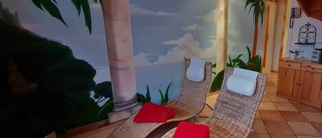 Una habitación con dos sillones de mimbre, una toalla roja sobre cada uno, y un mural con una escena tropical de palmeras y playa.