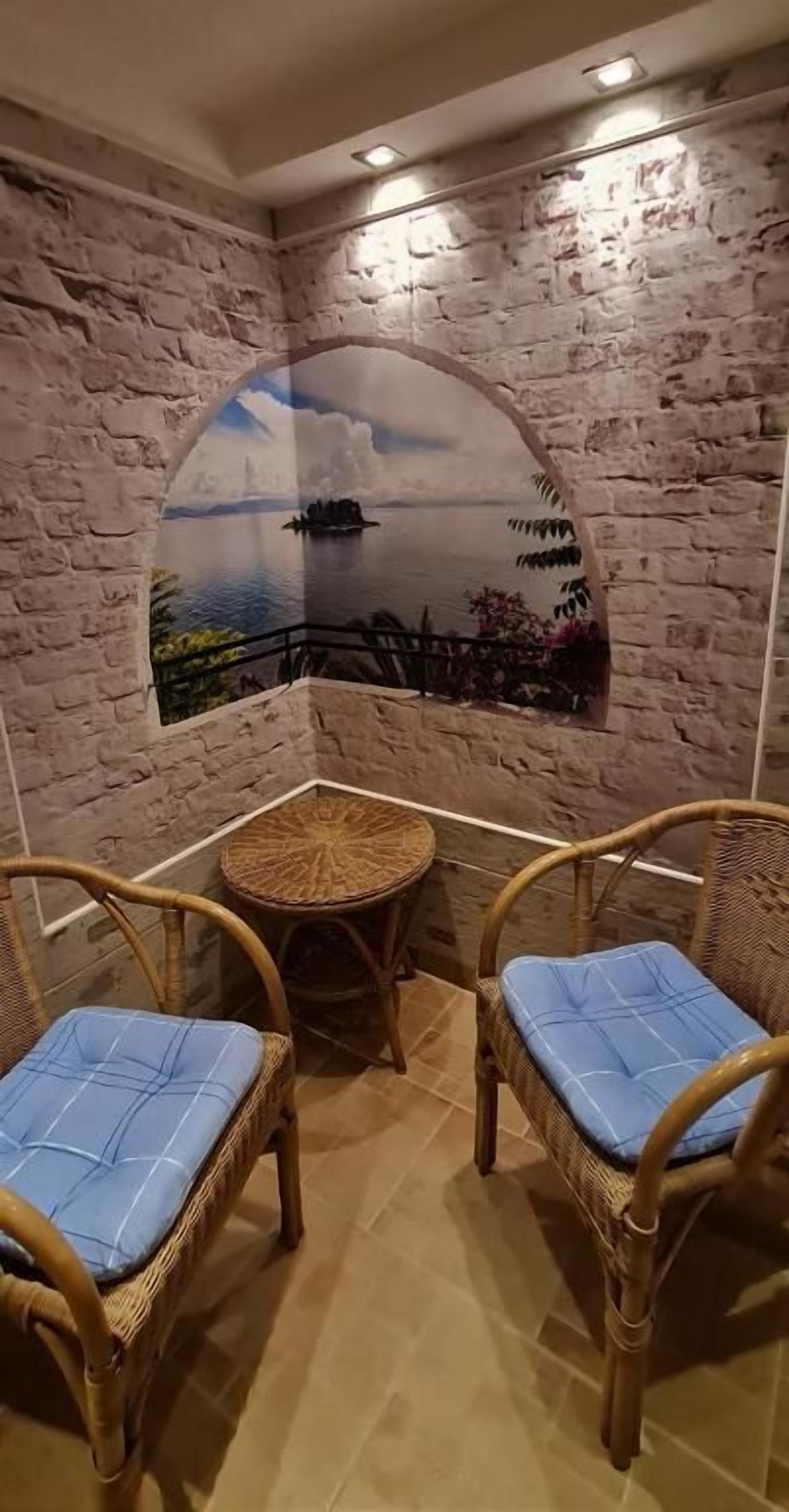 Une pièce d’angle avec un mur en briques, deux fauteuils en osier dotés de coussins bleus et une petite table ronde.