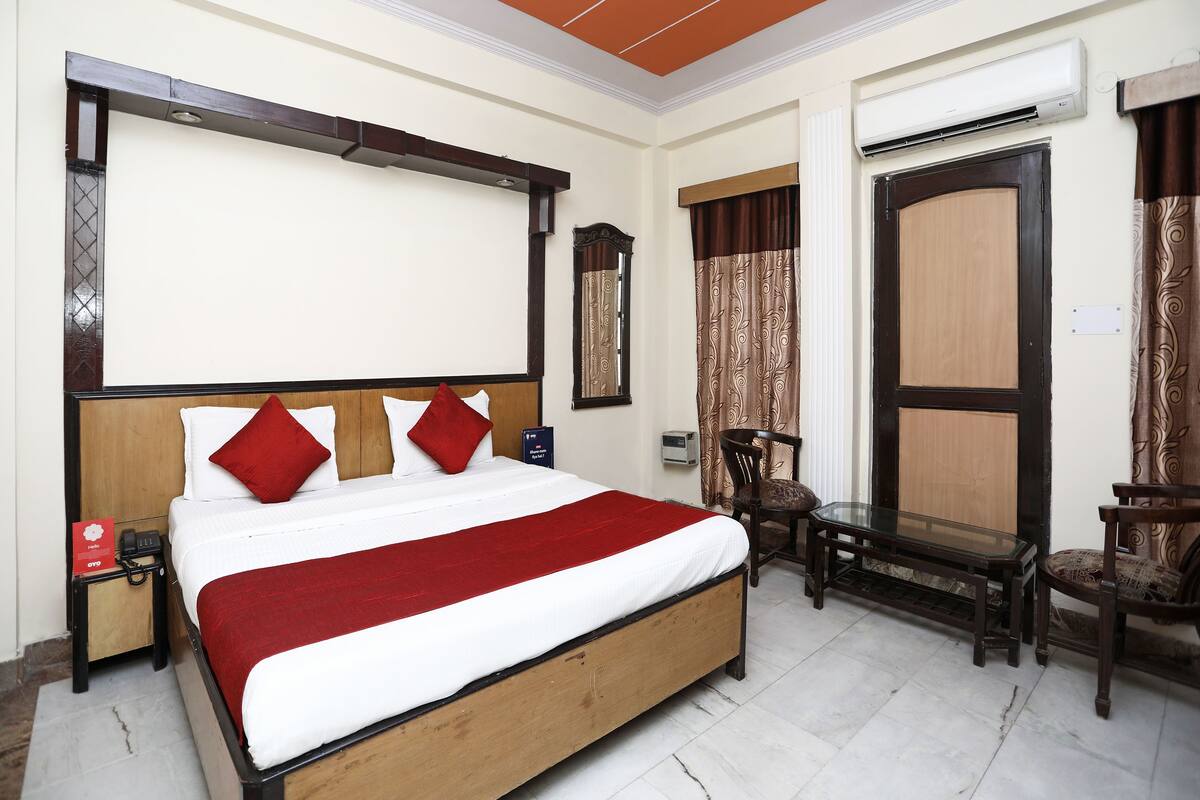 A hotel room with a bed, a desk, a chair, an air conditioning unit, and a ceiling fan.