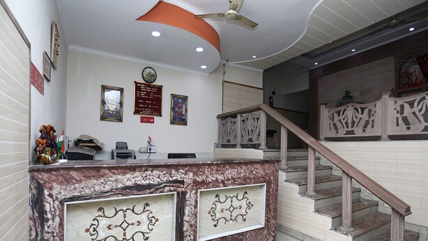 Un espace d’accueil avec un comptoir en marbre, une horloge, des tableaux encadrés et un escalier.