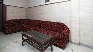 Une pièce avec un canapé à motifs floraux rouges, une table basse en verre et un tableau accroché au mur.