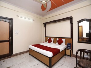 A hotel room with a wooden bed, red and white bedding, a ceiling fan, a mirror, and a nightstand with a book. - OYO 12671 Hotel Prithvi Palace (Ghaziabad)