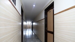 Un couloir aux murs recouverts de carreaux, au sol en marbre et aux portes en bois.