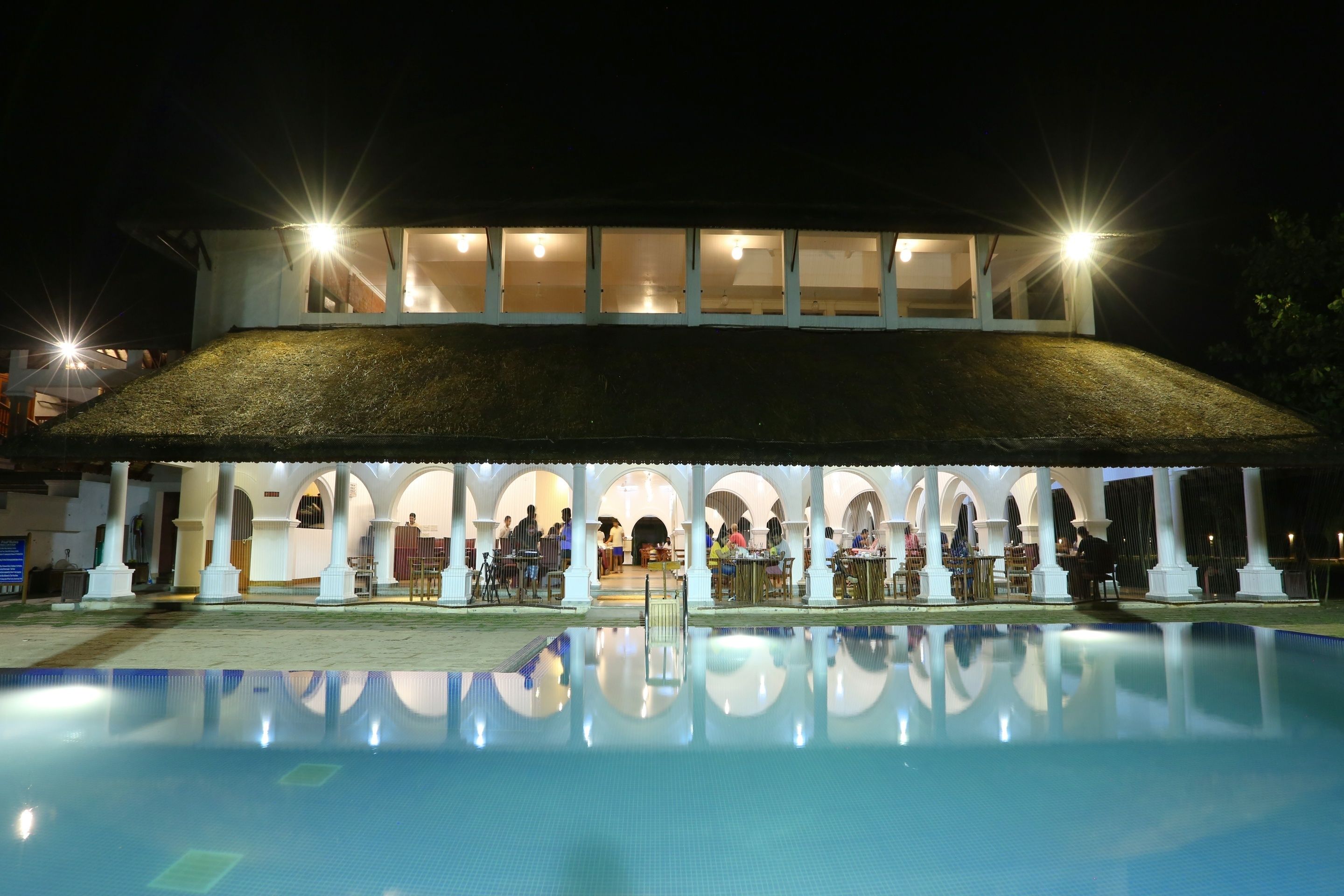 A hotel with a swimming pool, covered outdoor seating area, and a thatched roof structure.